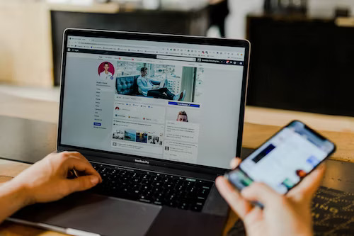 Person using laptop with social media marketing strategies for small businesses on cellphone screen